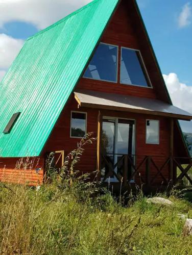 ein rotes Haus mit einem grünen Dach auf einem Hügel in der Unterkunft Linda cabaña en Puyehue con vista al volcán in Ñilque