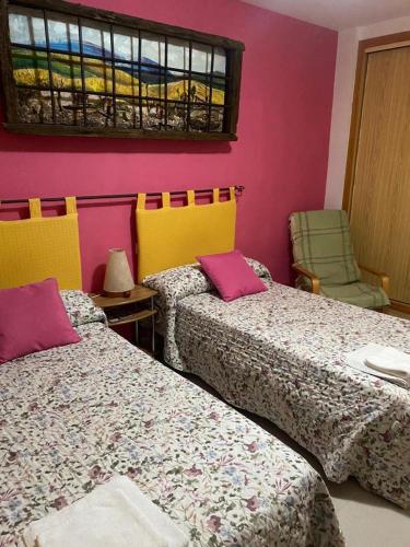 two beds in a room with pink and yellow at Hostal y Apartamentos la Vereda in Ruidera