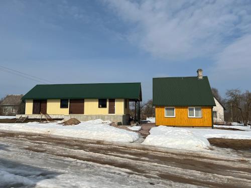 una casa amarilla con techo verde en la nieve en Brīvdienu namiņš en Ludza