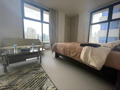 Schlafzimmer mit einem Bett, einem Tisch und Fenstern in der Unterkunft Heart of Abu Dhabi - Adorable Master Room in Abu Dhabi