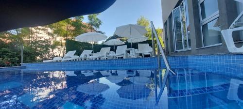 a pool with white chairs and umbrellas next to a building at Apartmani Matin Breg in Jošanička Banja