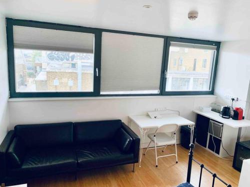 a living room with a black couch and two windows at Designer Room with Private Bathroom in London