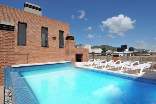 a swimming pool with chairs and a brick building at AVIS Departamentos peatonal in Villa Carlos Paz