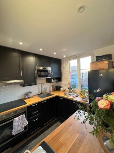 a kitchen with black cabinets and a wooden table at Vanves : 2 pièces lumineux aux portes de Paris in Vanves