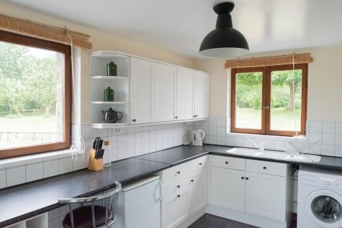 La cuisine est équipée de placards blancs, d'un évier et de fenêtres. dans l'établissement Le jardin des oiseaux – Escapade nature, à Saint-Georges-de-Reintembault