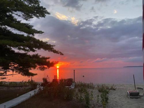 a sunset on the beach with a lighthouse in the water at The Huron Hutch in Evergreen Shores
