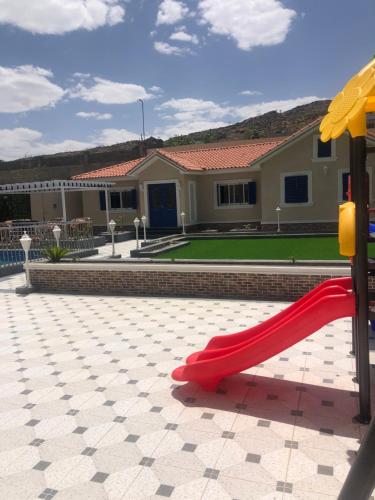 a playground with a red slide in front of a house at شاليه الشروق in Ash Shuqra