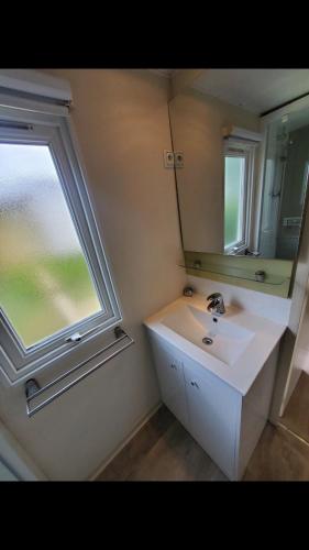 une salle de bain avec un lavabo, un miroir et une fenêtre dans l'établissement Charmant Mobil home 6 places, à Carnac