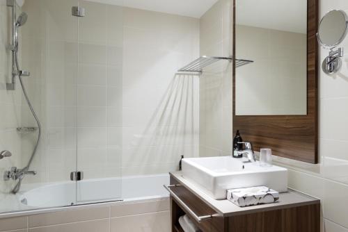 a white bathroom with a sink and a shower at Aparthotel Adagio La Defense Courbevoie in Courbevoie