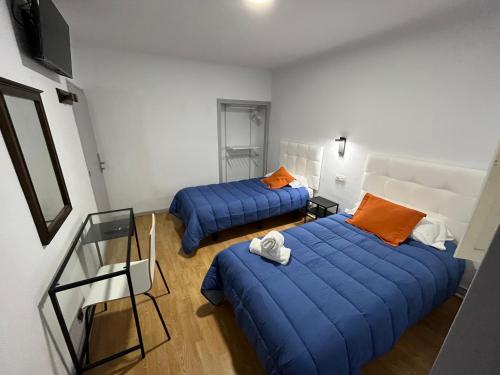 2 Betten in einem Zimmer mit blauer Bettwäsche und orangefarbenen Kissen in der Unterkunft Hostal ARS in Puigcerdà