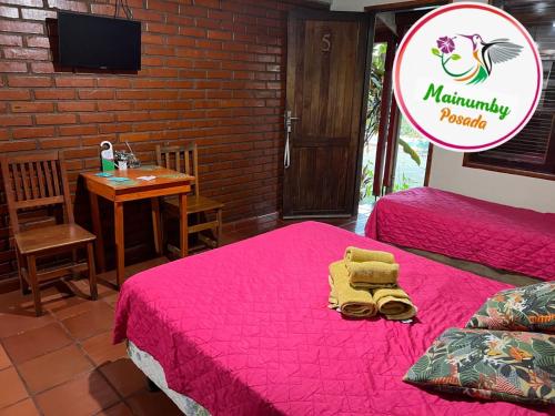 a room with two beds and a table and a sign at Mainumby- Colibri Posada in Puerto Iguazú