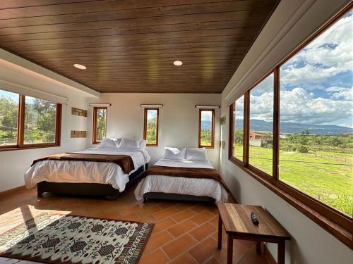 a bedroom with two beds and windows and a table at Hotel Pliosaurio Campestre in Villa de Leyva