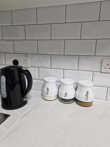 a black tea kettle and three cups on a kitchen counter at Pav's Den in Ince-in-Makerfield