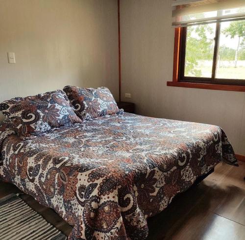 a bedroom with a bed with a flowered blanket on it at Cabaña Refugio Eluney in Villarrica