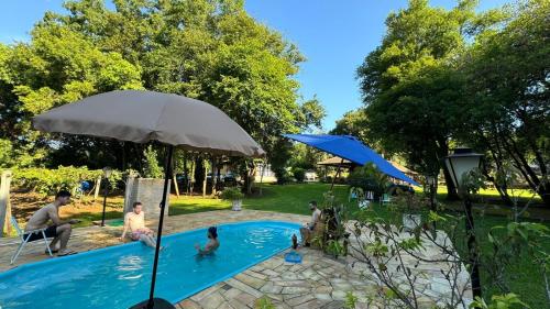 a group of people in a swimming pool with an umbrella at Casa de campo Quinta do Floriano in Teutônia