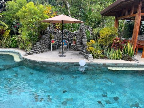 a table and chairs under an umbrella next to a swimming pool at Sloth Premium Riverfront Jungle Villa with Jacuzzi and Pool in Uvita