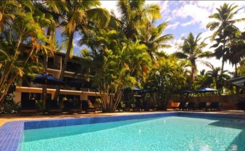 a swimming pool in front of a resort with palm trees at Oasis Palms Hotel in Nadi