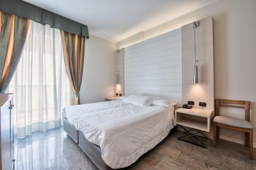 una camera con un grande letto bianco e una sedia di Hotel Columbus a Lignano Sabbiadoro