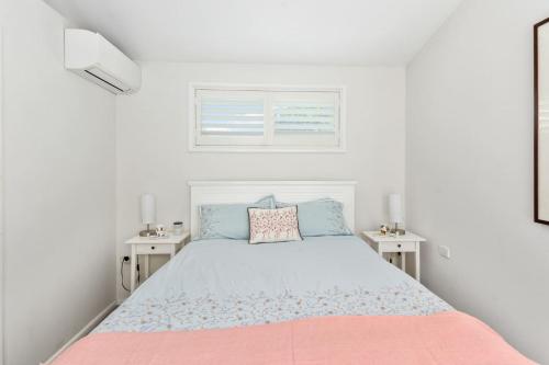 a white bedroom with a bed and two tables at Keiraville Poolside Escape - University Proximity in Keiraville