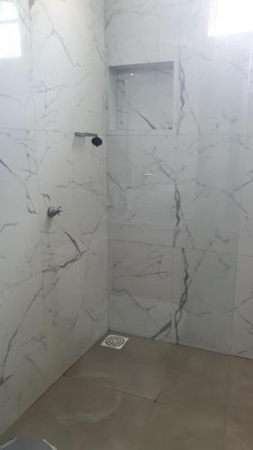 y baño con ducha y paredes de mármol blanco. en Residencial Mirandinha en Boa Vista