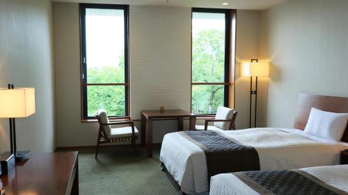 a hotel room with two beds and a desk and two windows at Chion-in Wajun Kaikan in Kyoto
