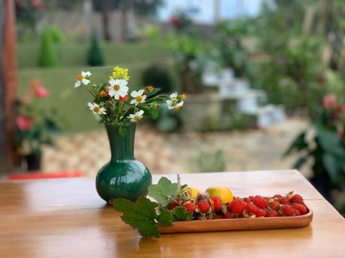 un jarrón verde con flores y fresas sobre una mesa en MANG DEN Romantic, en Kon Von Kla