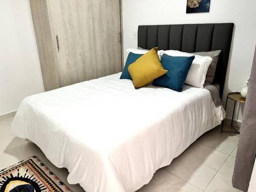 een wit bed met blauwe en gele kussens erop bij Enchanted Sabaneta Condo in Sabaneta