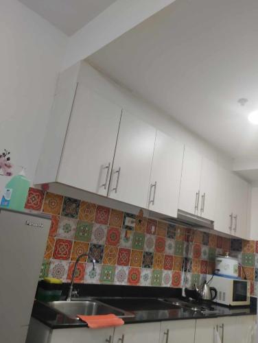 a kitchen with white cabinets and a tile back splash at Staycation at moa in Manila