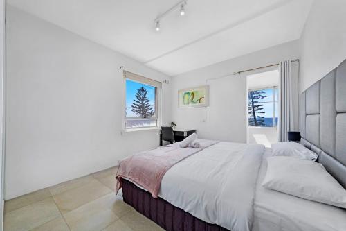 a white bedroom with a large bed and two windows at Ocean View 1 bedroom Private Apartment next to Maroubra Beach in Sydney