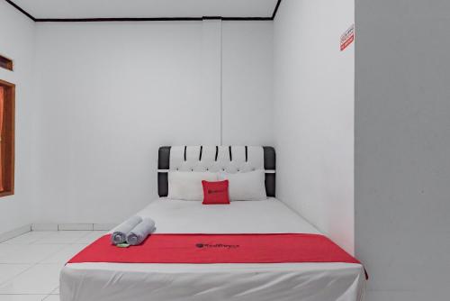 a bed in a white room with a red blanket at RedDoorz @ Geopark Ciletuh Sukabumi in Cilowa