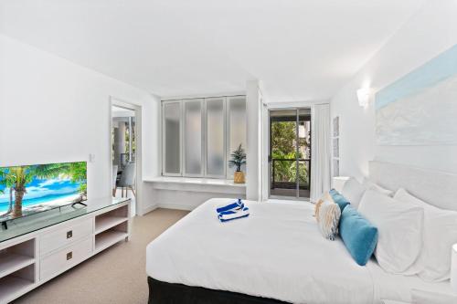 a white bedroom with a large bed and a flat screen tv at Belle Escapes Drift Beachfront Resort Suite 1305 in Palm Cove