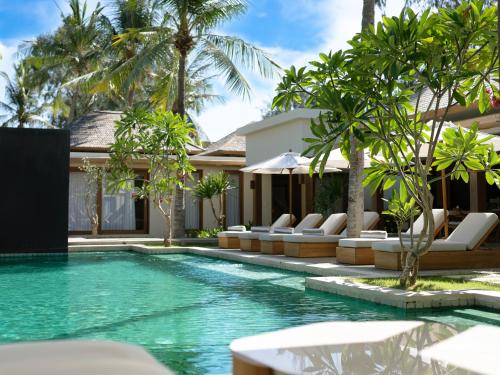 une piscine avec des chaises longues et une villa dans l'établissement Cocana Resort Gili Trawangan, à Gili Trawangan