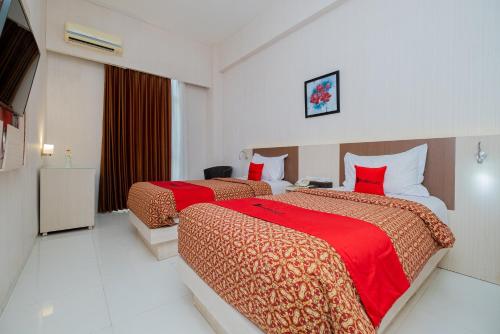 two beds in a hotel room with red sheets at RedDoorz Premium @ Jalan Veteran Bojonegoro in Bojonegoro