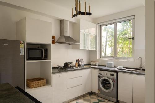 a white kitchen with a washing machine and a window at El Sereno 2 BHK Stylish Apartments In Vagator with Garden and Pool- 10 minutes drive to Vagator Beach in Chapora