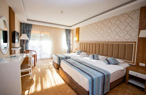 a hotel room with two beds and a desk at Kustur Club Holiday Village - All Inclusive in Kusadası