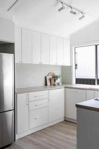 a white kitchen with white cabinets and a refrigerator at Casa Wilde in the Hunter in Cessnock