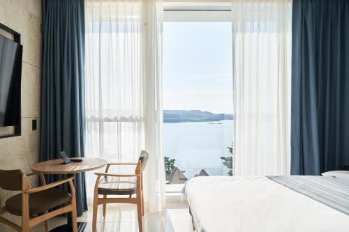 a bedroom with a bed and a table and a large window at Yeosu Calacatta Hotel & Resort in Yeosu