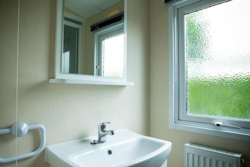 La salle de bains est pourvue d'un lavabo, d'un miroir et d'une fenêtre. dans l'établissement Recreatiepark Duinhoeve 12, à Udenhout