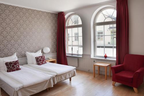 Cette chambre d'hôtel comprend deux lits et un fauteuil rouge. dans l'établissement Clarion Collection Hotel Bolinder Munktell, à Eskilstuna