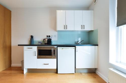 cocina con armarios blancos y microondas en Notting Hill Serviced Apartments by Concept Apartments, en Londres