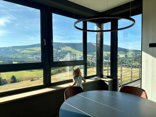 a little girl sitting at a table looking out of a window at Boutique apartment Heidi with mountain view in Loučná pod Klínovcem