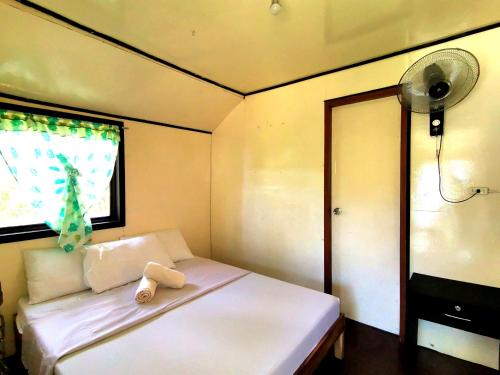 a small bedroom with a white bed with a fan at Villa Milanel Port Barton in Port Barton
