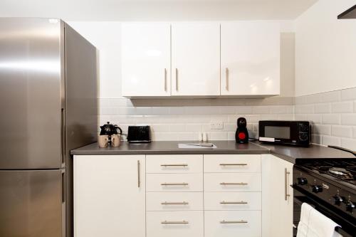 cocina con armarios blancos y nevera de acero inoxidable en Suite 3 - Stunning Room in Oldham Sociable House en Oldham