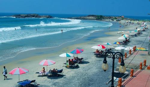 a beach with umbrellas and people sitting on the sand at Beach Villa Kovalam in Kovalam