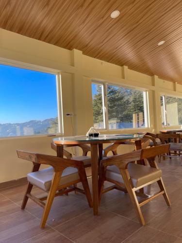 a dining room with a table and chairs and windows at The Deodar Stays in Kanatal
