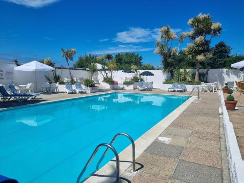 a large blue swimming pool with chairs and palm trees at Pine Lodge in Newquay