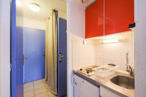 La cuisine est équipée de placards rouges et bleus et d'un évier. dans l'établissement Les Aiguilles d'Arves - Vue montagne à au Corbier, à Villarembert