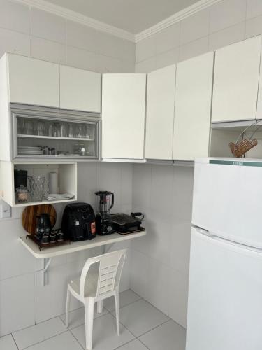 a white kitchen with a chair and a white refrigerator at Apartamento frente mar Guarujá Pitangueiras pé na areia in Guarujá