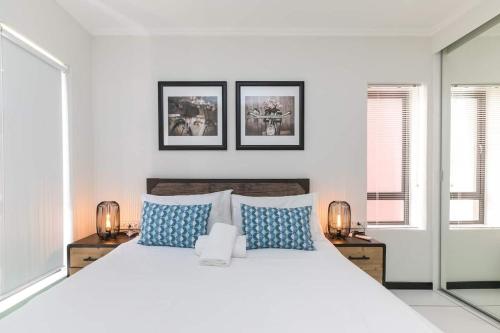 a white bedroom with a large bed with blue pillows at Nova Luxury Suites Fourways in Johannesburg