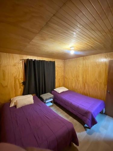 2 Betten in einem Zimmer mit lila Bettwäsche in der Unterkunft Cabaña Los Ulmos in Castro